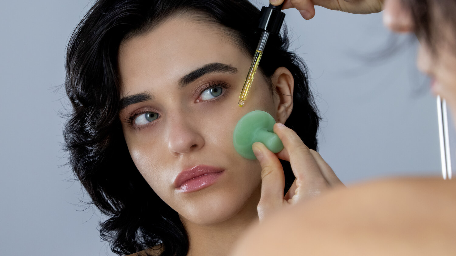 Soin visage - Femme se regarde dans le miroir avec l'huile de péridot et une pierre de massage