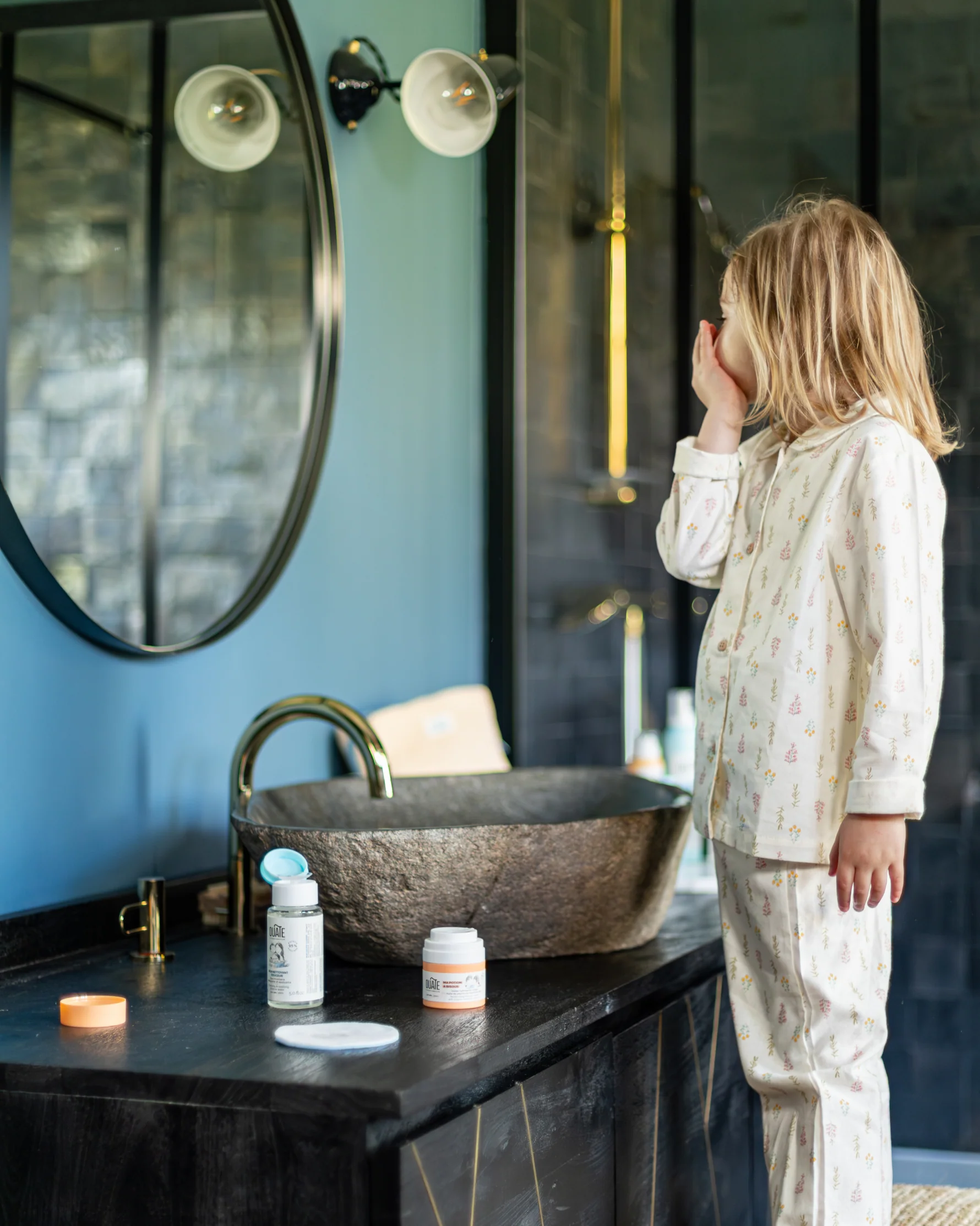 Enfant prenant soin de sa peau en nettoyant et hydratant son visage devant le miroir