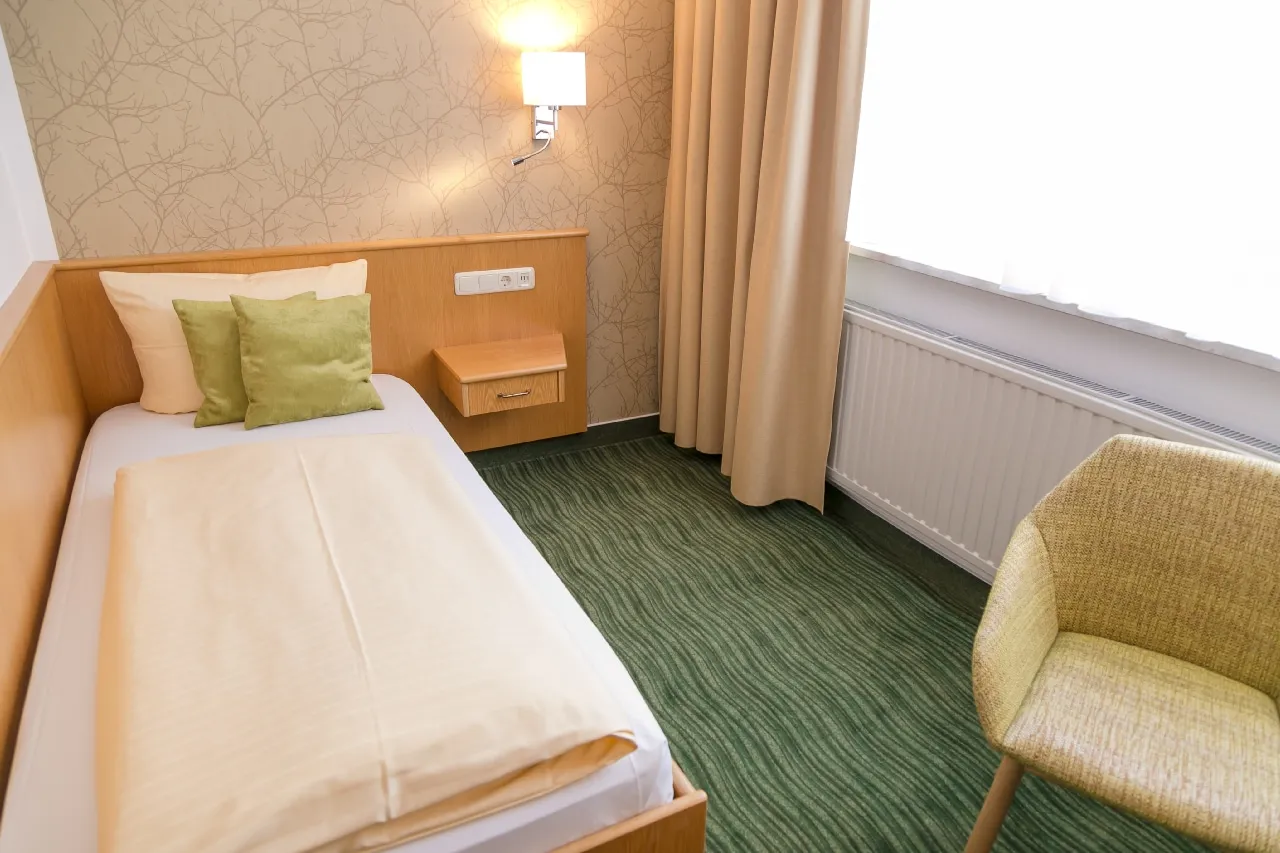 Modern eingerichtetes Hotelzimmer mit Einzelbett, Stuhl und großem Fenster.