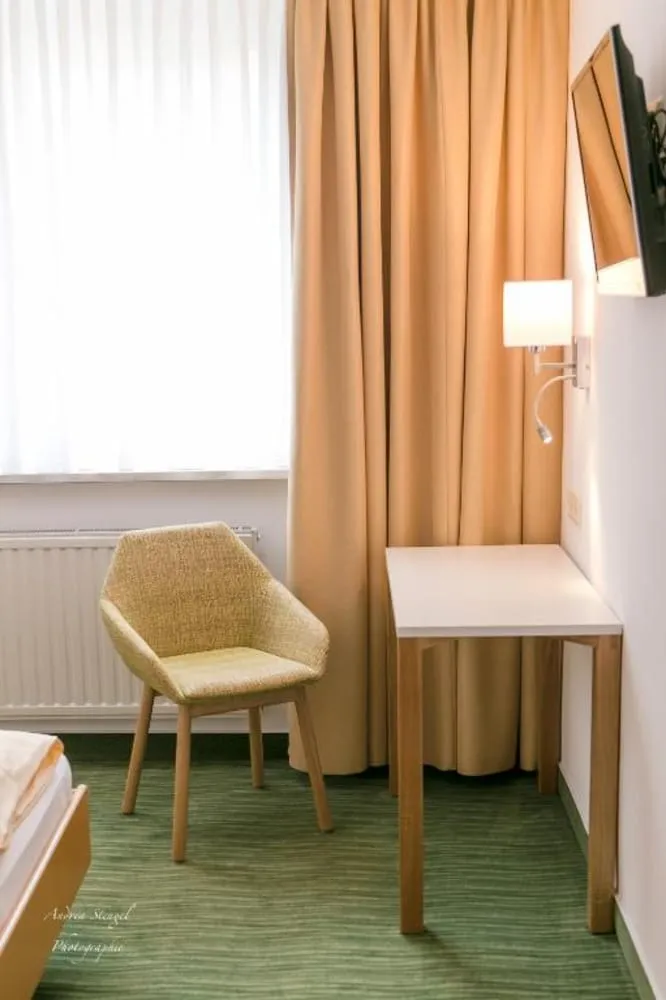 Heller Hotelzimmerbereich mit Stuhl, Schreibtisch und Vorhängen.
