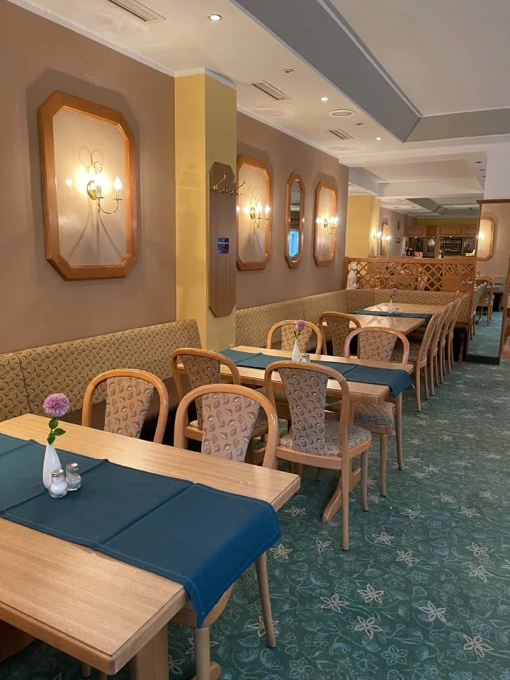 Elegantes Restaurant mit gedeckten Tischen, blauen Teppichen und warmem Wandlicht.
