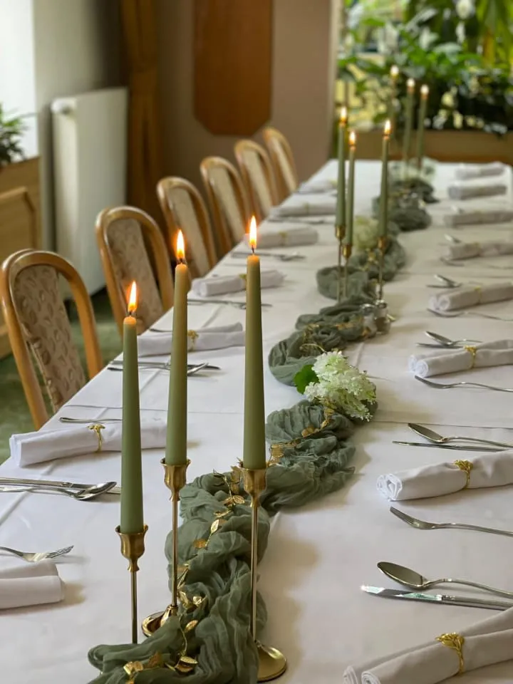 Festlich gedeckter Tisch mit weißen Tischdecken, goldenen Kerzenhaltern und grüner Tischdekoration.