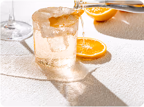 Cóctel con rodaja de naranja sobre mantel blanco, refrescante y brillante