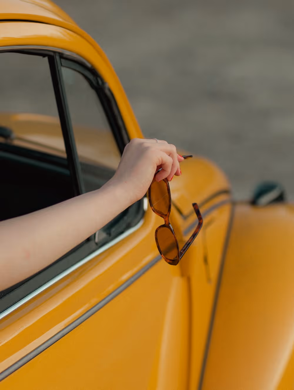 Käsi pitelee ruskeita aurinkolaseja keltaisen taustaelementin edessä kuvastaen Stooren kirkasta näkökulmaa ja tarinallista brändistrategiaa