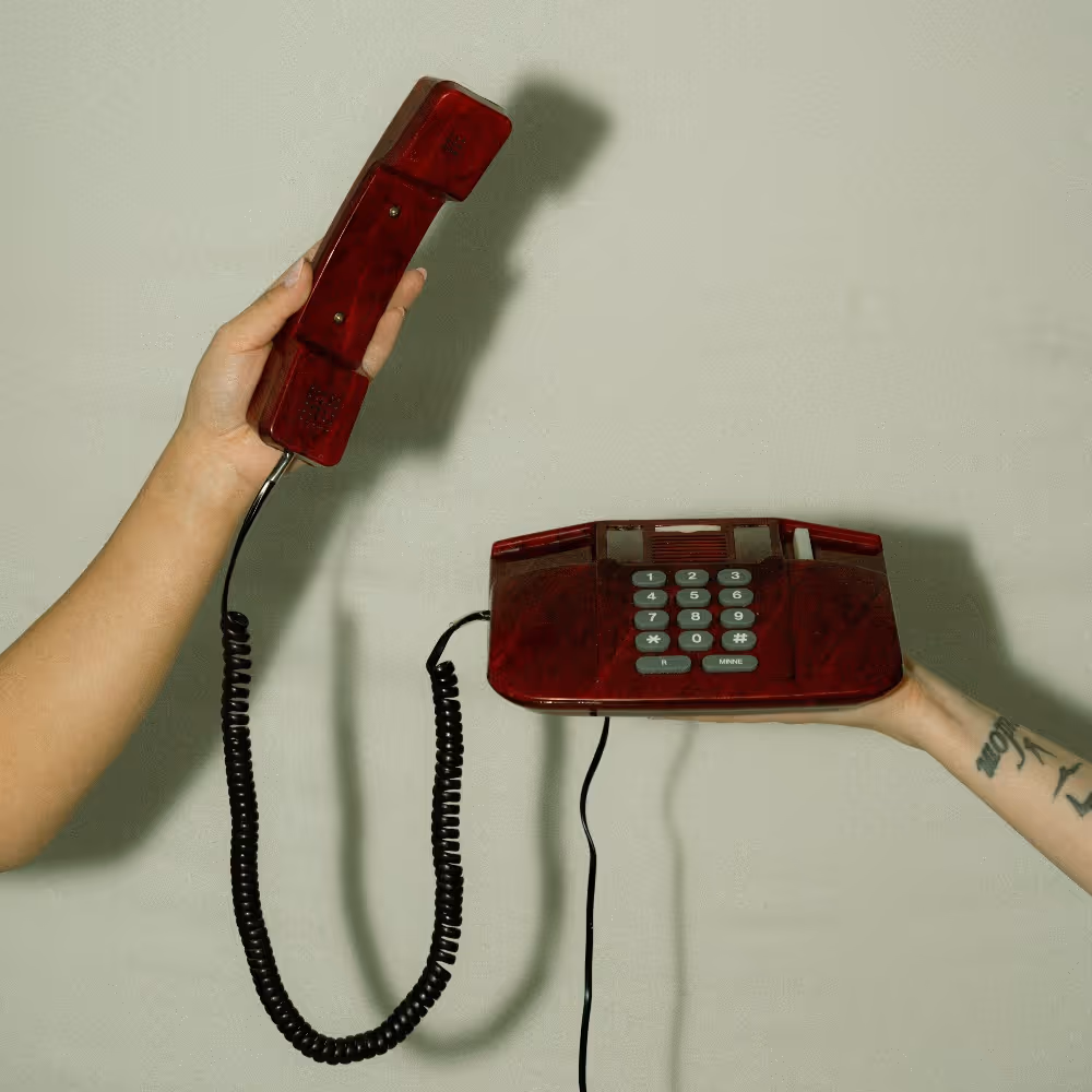 Käsi nostaa Stooren punaista lankapuhelinta vaaleaa taustaa vasten, kutsuen yrityksiä aloittamaan yhteisen markkinointitarinan
