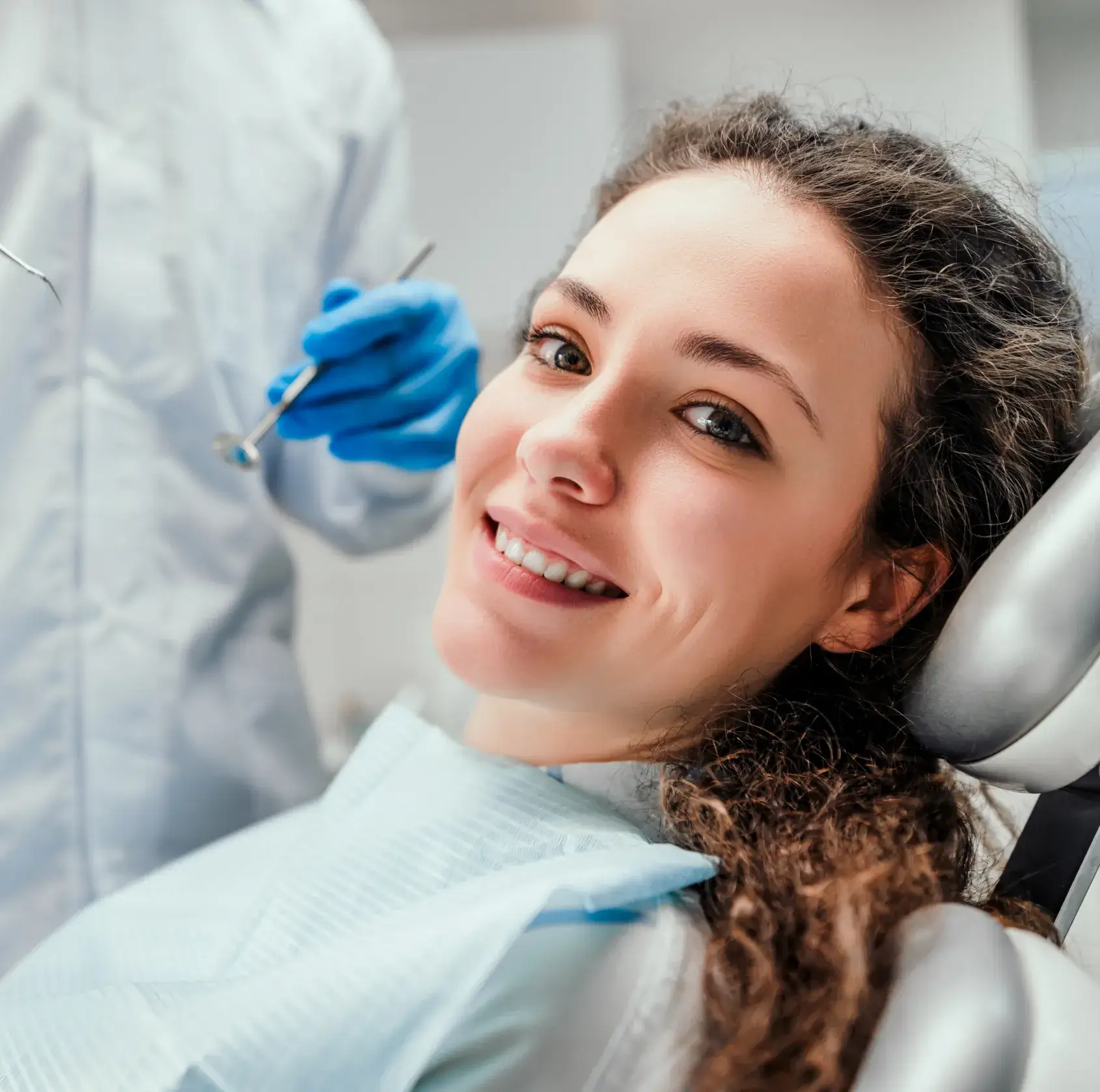 A woman sitting in a dentist chair with a toothbrush in her mouth.