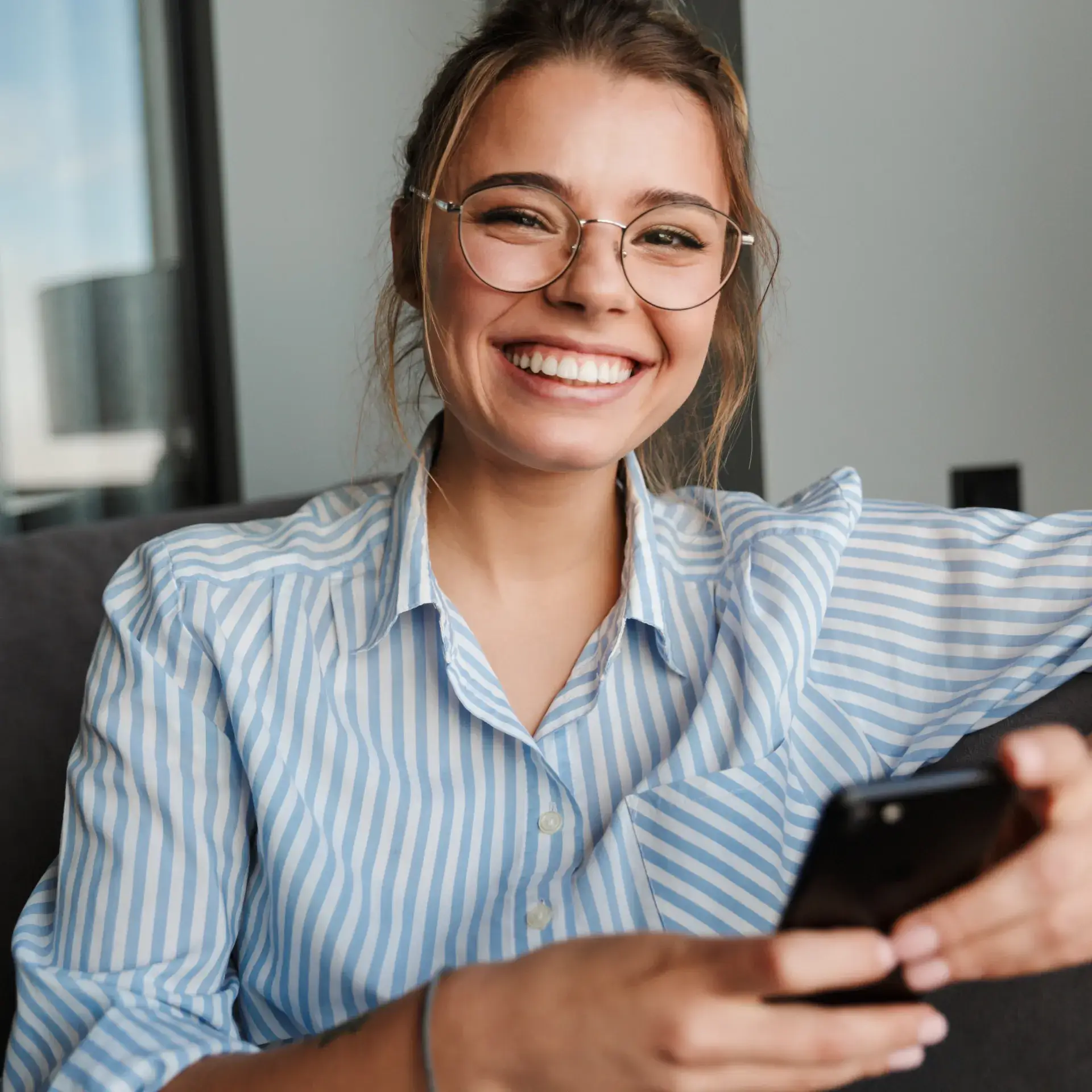 A woman wearing glasses is looking at her cell phone.