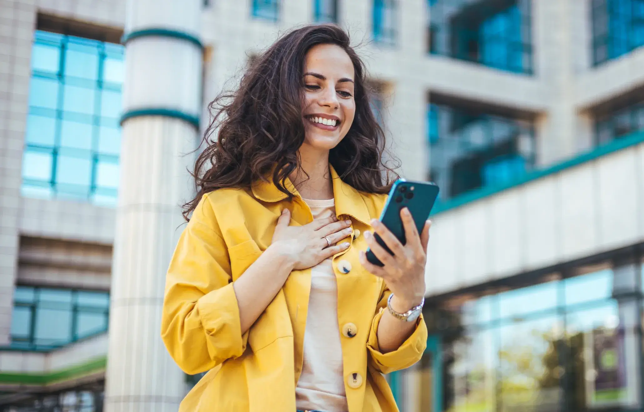 A woman in a yellow jacket looking at her cell phone.
