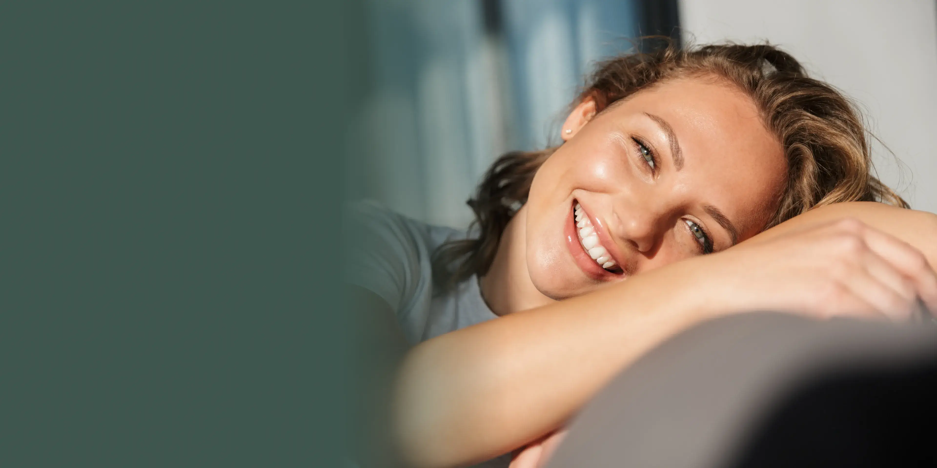 A woman is smiling and leaning on a couch.