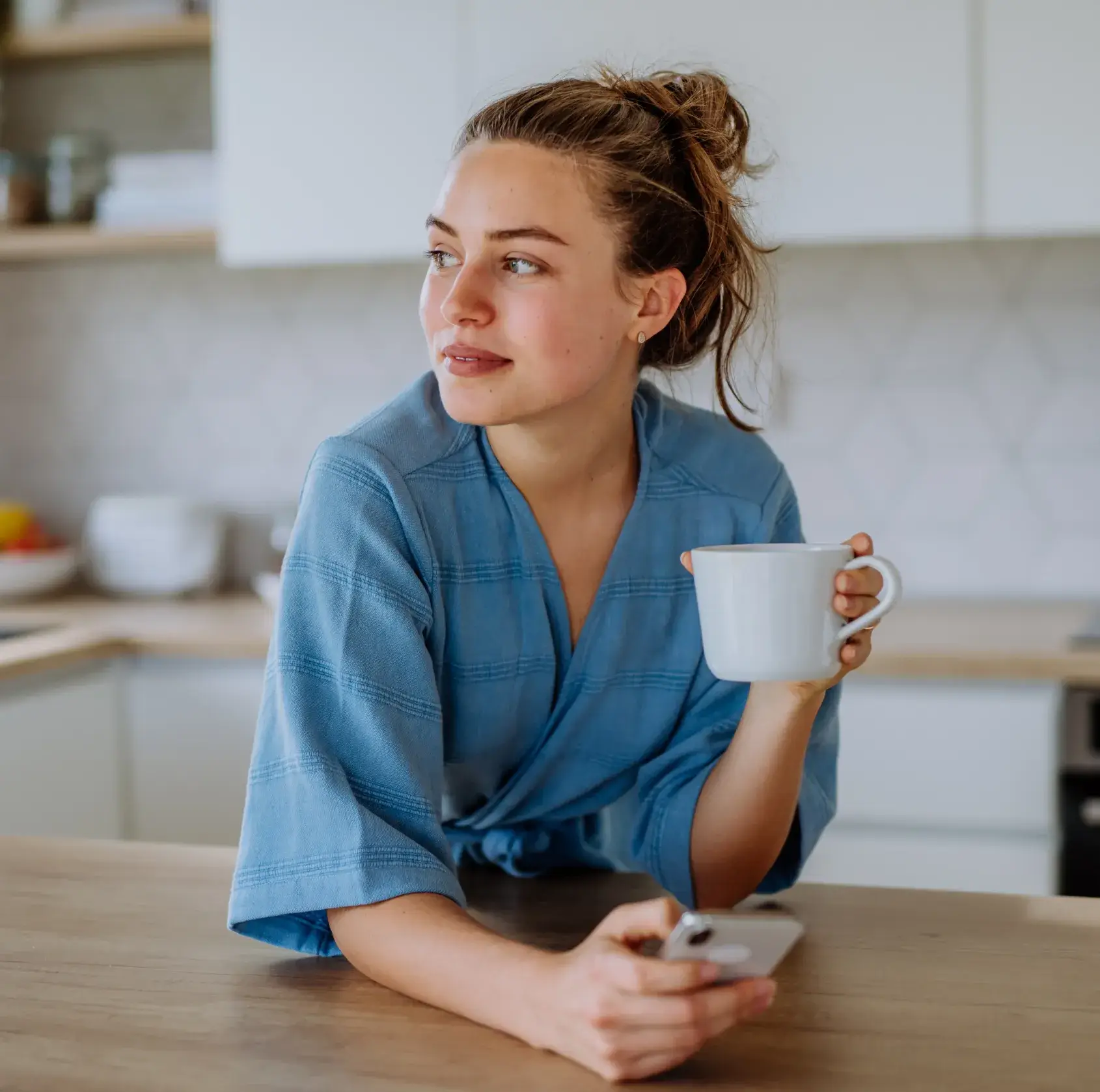 A woman sitting at a table holding a cup and a remote control.