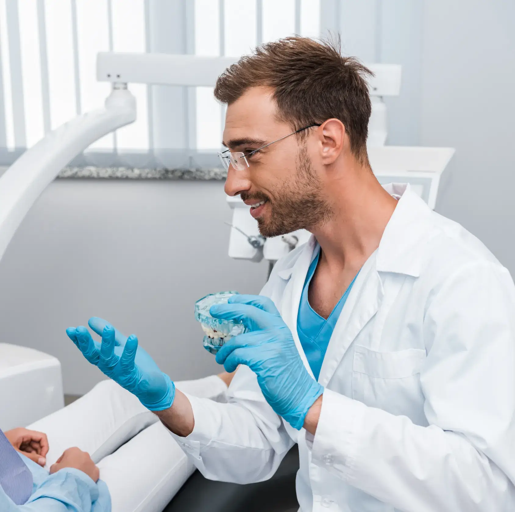 A man in a white lab coat and blue gloves holding a toothbrush.