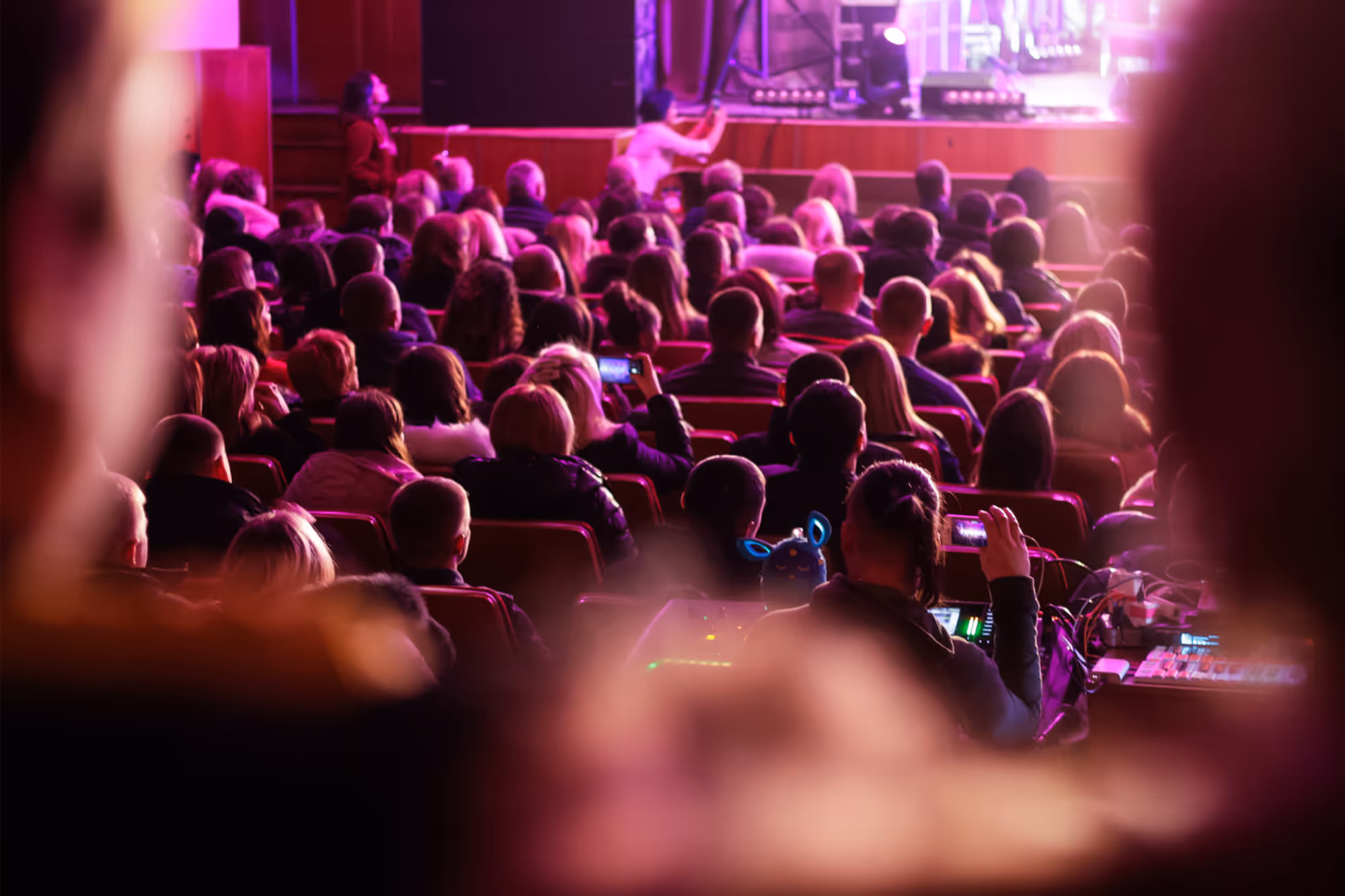 An audience seated in a dark theater watching a performance on a brightly lit stage.