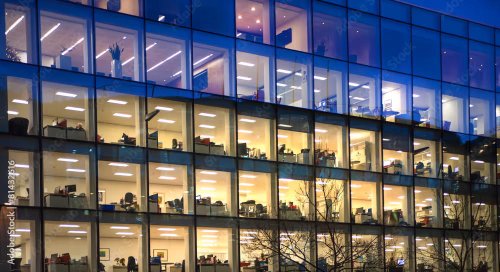 An office building at night with illuminated windows showing people working.