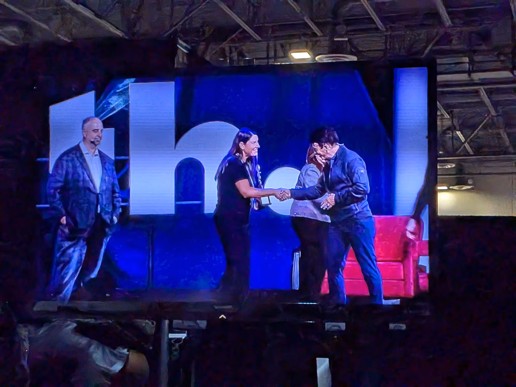 A group onstage during an event, shown on a large screen to the audience.