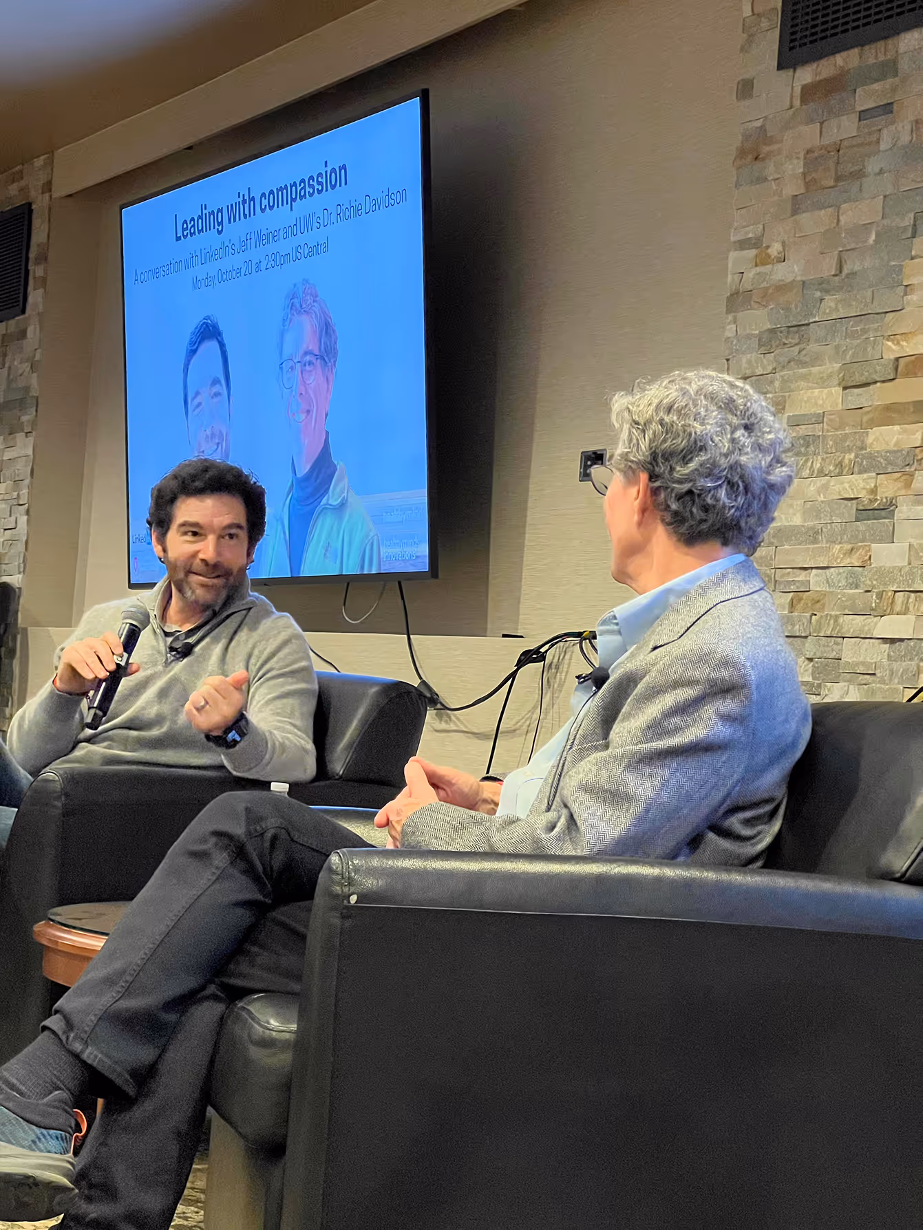 Two men seated onstage having a discussion during a live talk.