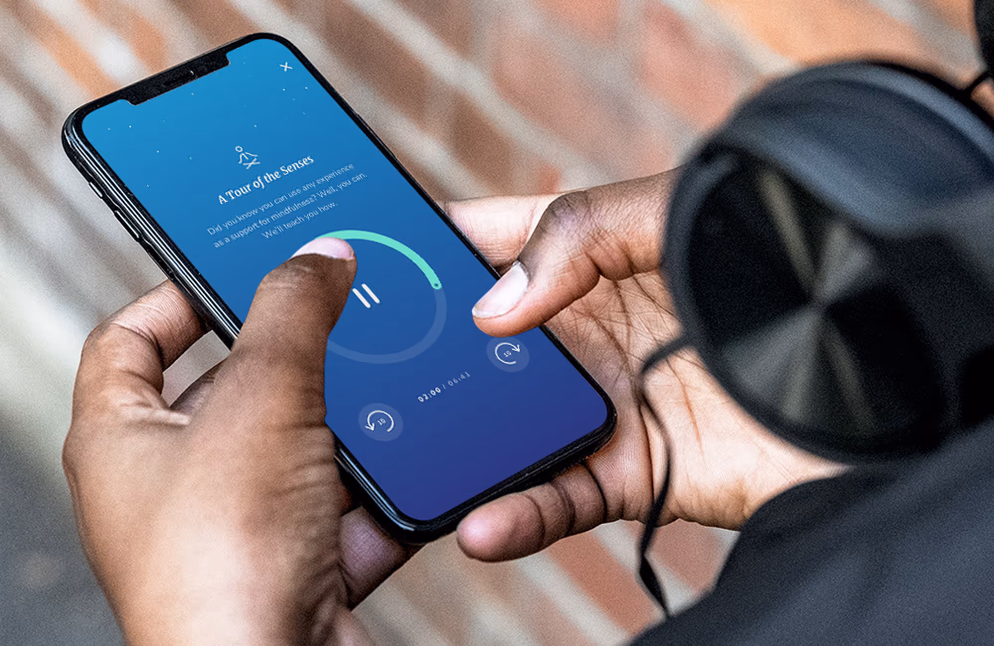 Hands holding a smartphone showing a mindfulness audio session on a blue app interface.