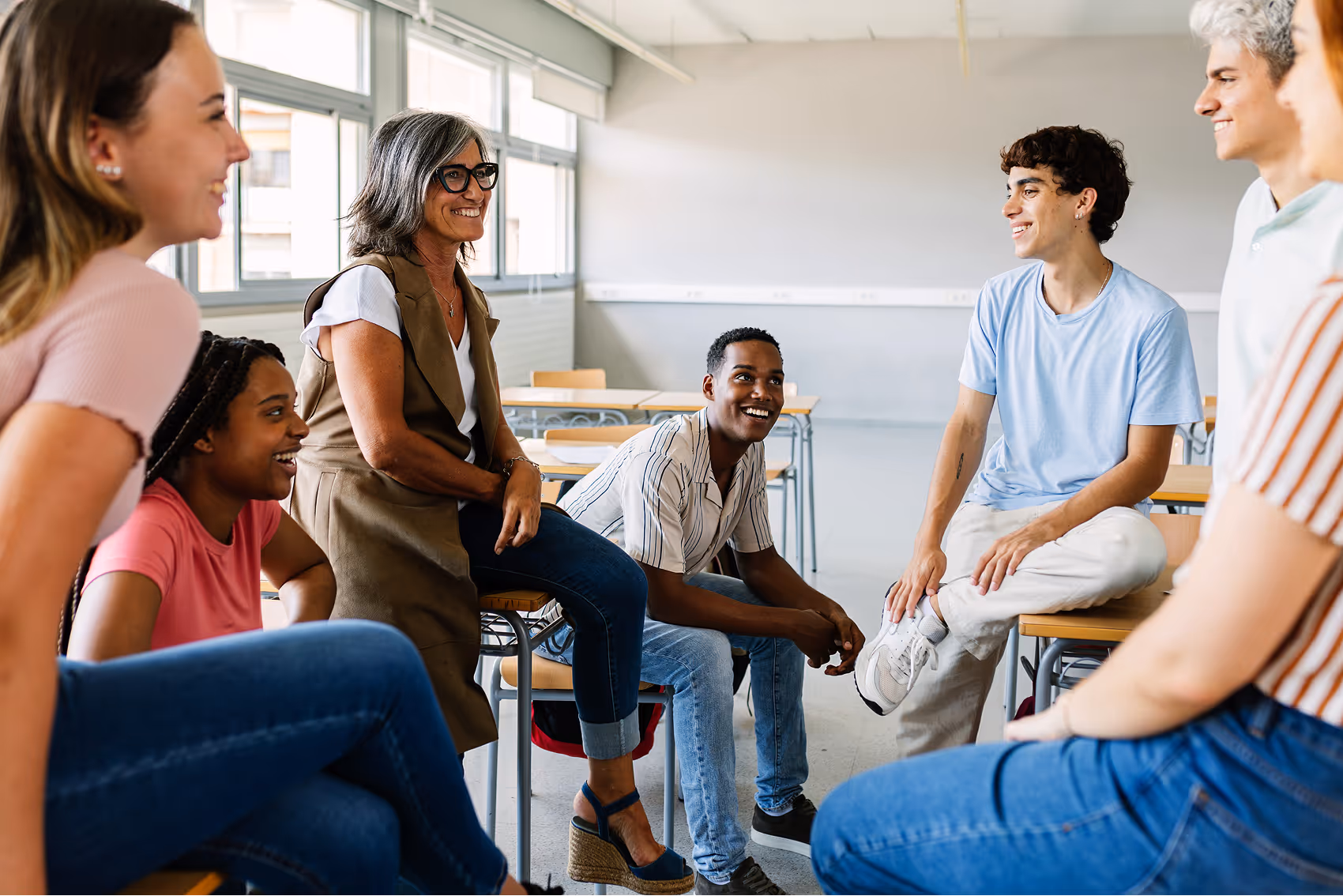 A teacher sitting with high school students in a circle leading a classroom discussion.