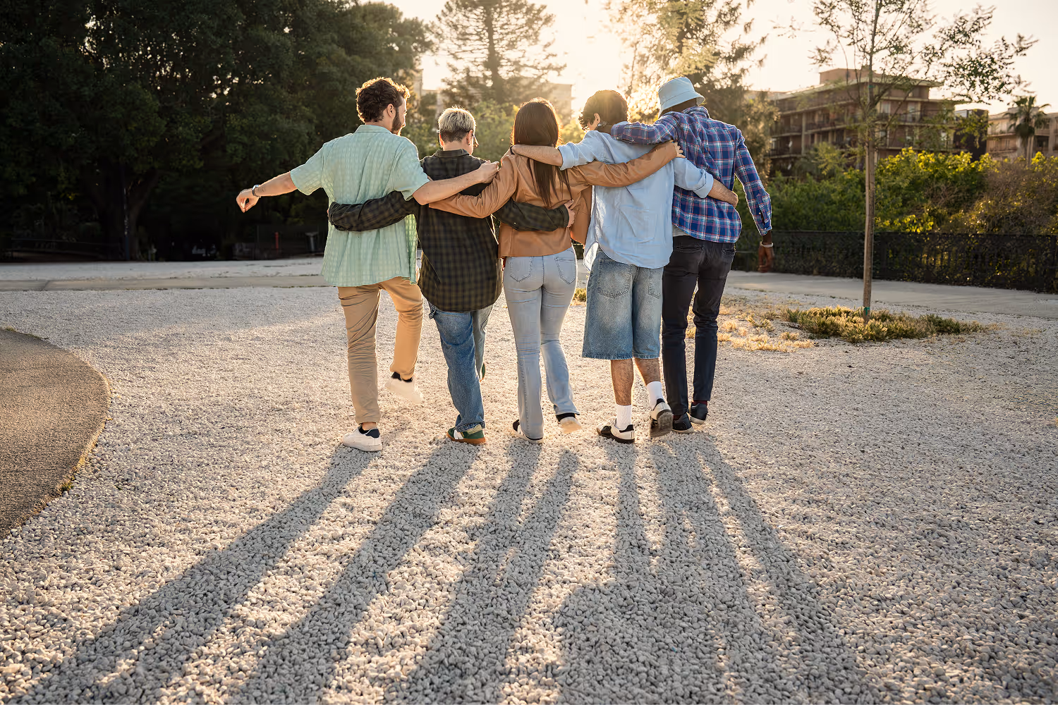 A group of friends walking arm in arm down a gravel road at sunset.
