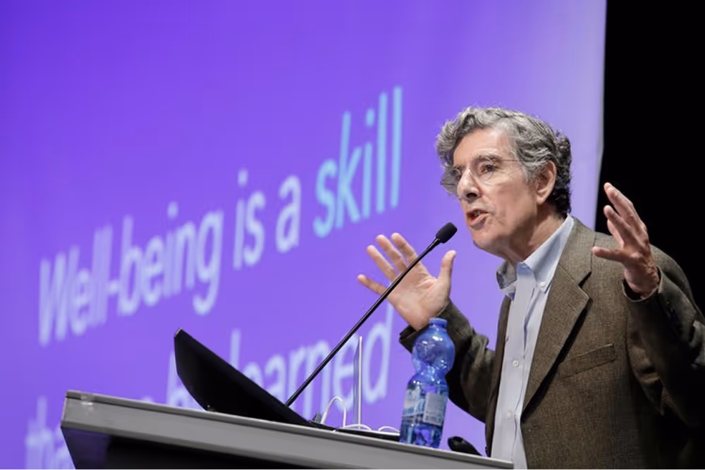Richard J. Davidson presenting onstage at a conference, gesturing while discussing well-being as a skill.