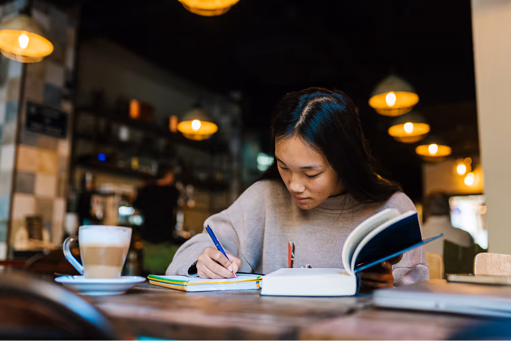 A woman writing in a notebook while studying in a cozy café.