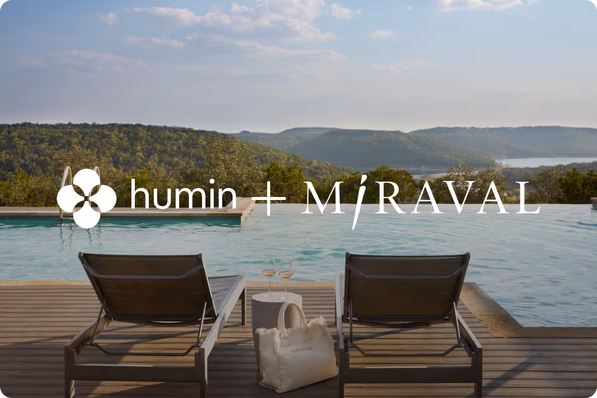 Two empty lounge chairs beside an infinity pool overlooking a scenic forested valley and distant water body under a partly cloudy sky.