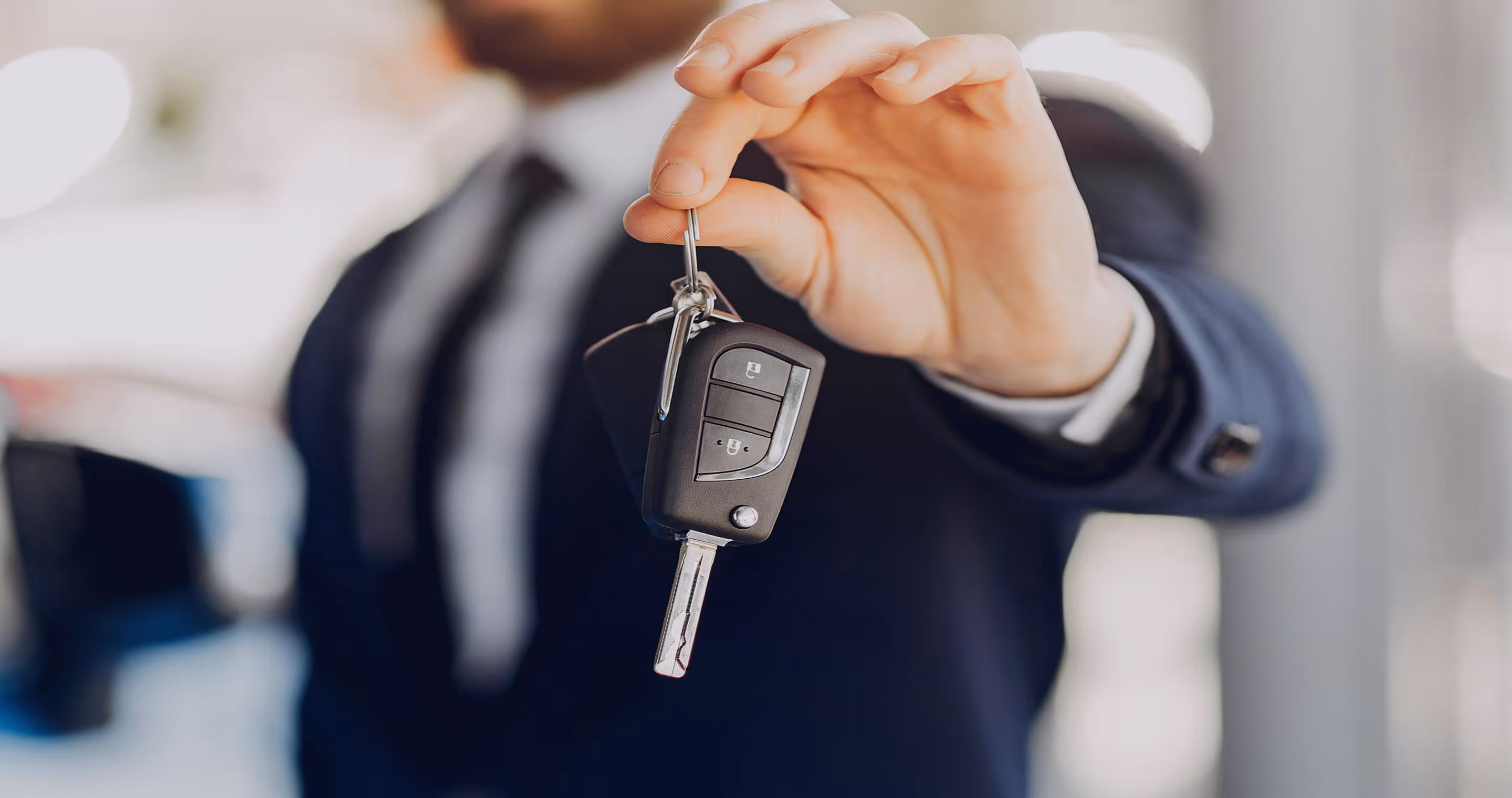 A man in a suit holding a car key.
