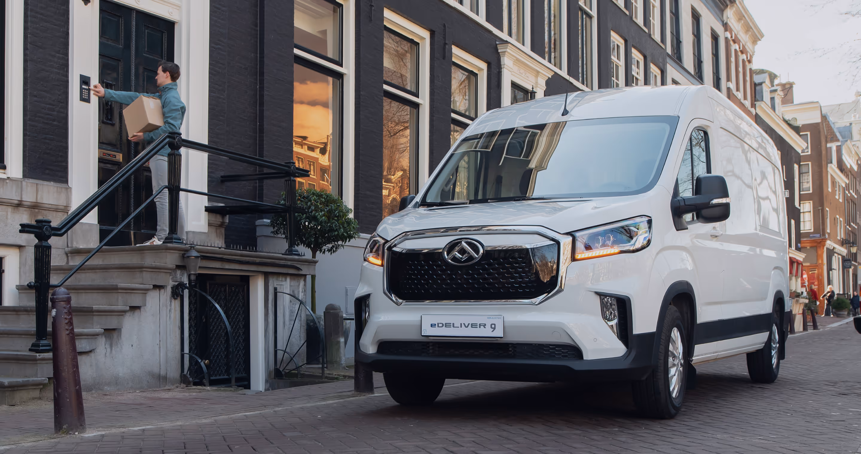 Person holding a box pressing a doorbell at a black door beside a white eDeliver 9 electric delivery van on a city street.