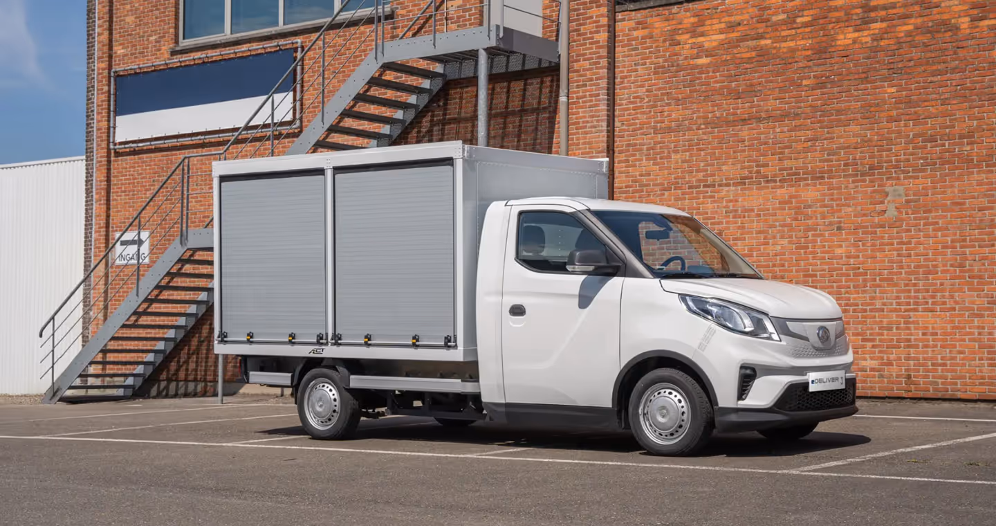 White delivery truck with closed gray cargo box parked in front of a brick building with an external metal staircase.