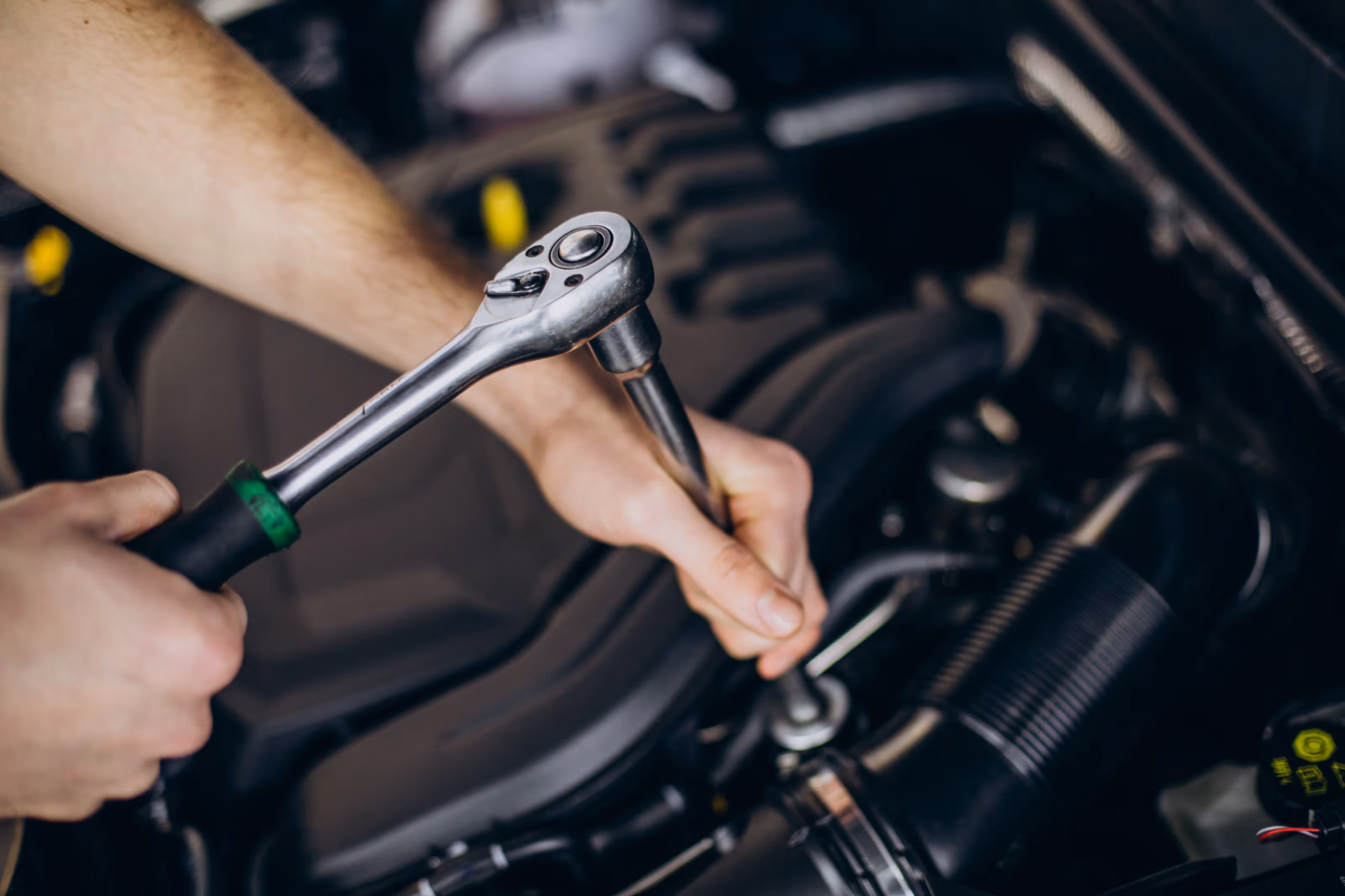 Close-up of hands using a ratchet wrench to tighten or loosen a bolt in a car engine.