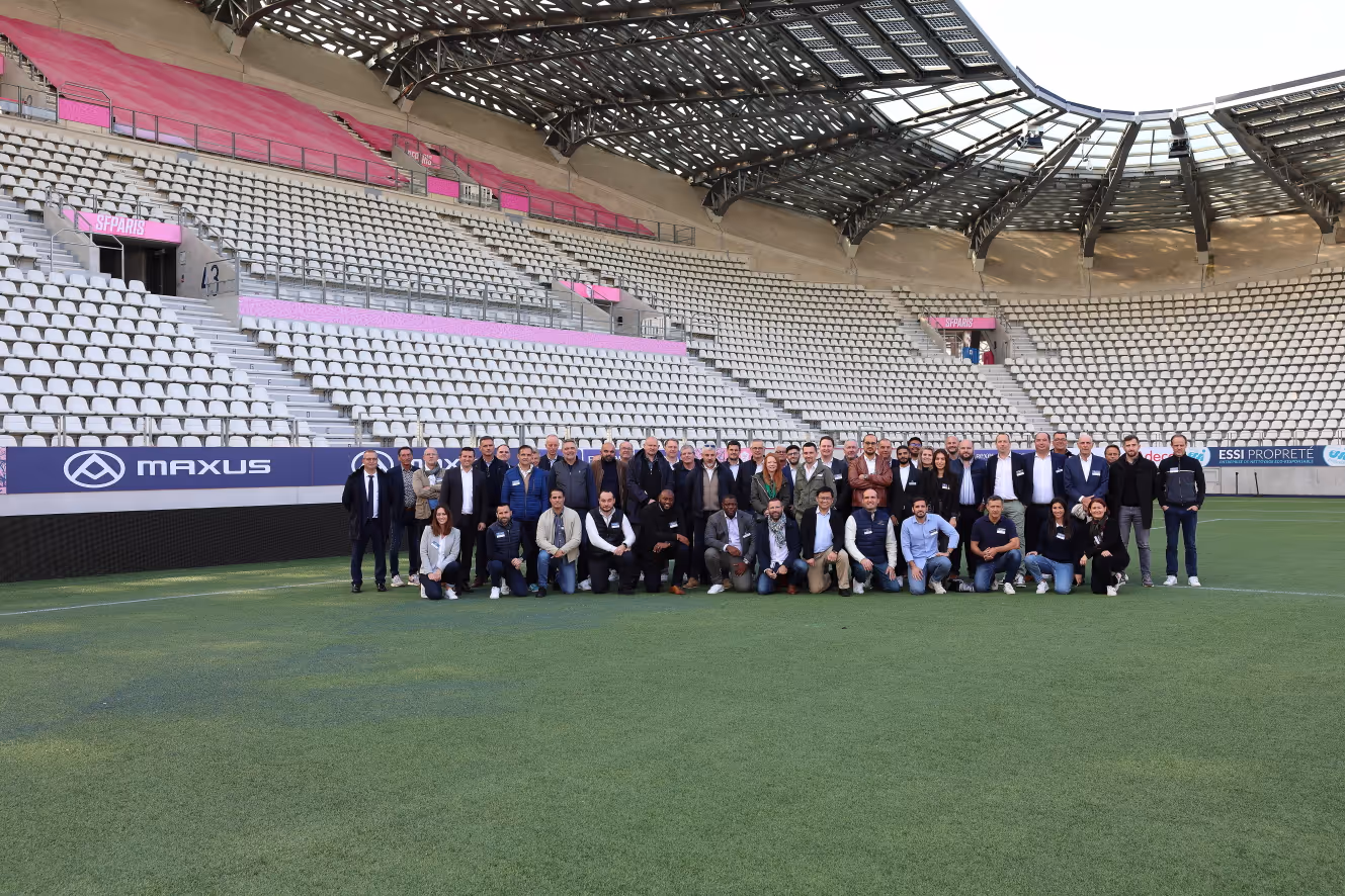 Group of people posing on a soccer field inside a large stadium with empty seats and a partially covered roof.