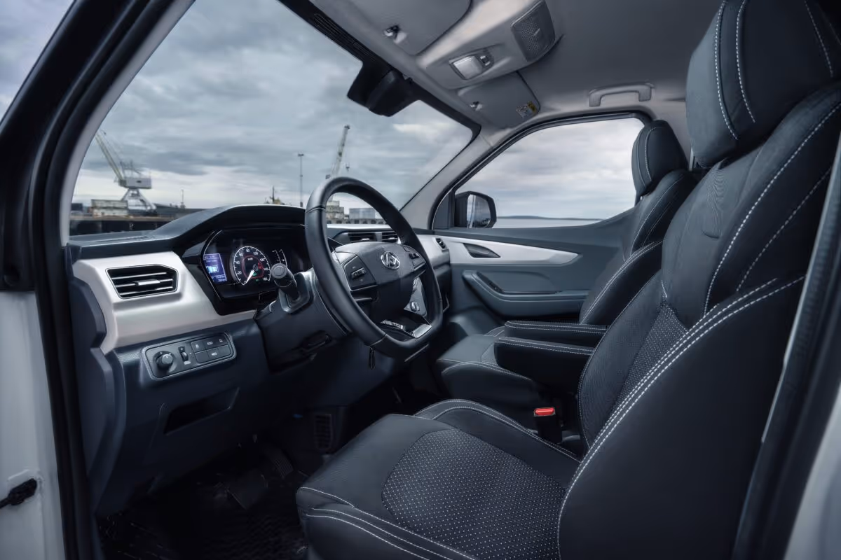 Interior view of a modern vehicle showing the steering wheel, dashboard, and black front seats with white stitching.