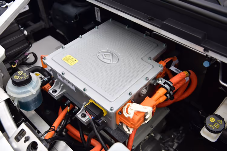Close-up of an electric vehicle's battery control unit with orange high-voltage cables connected inside the engine compartment.
