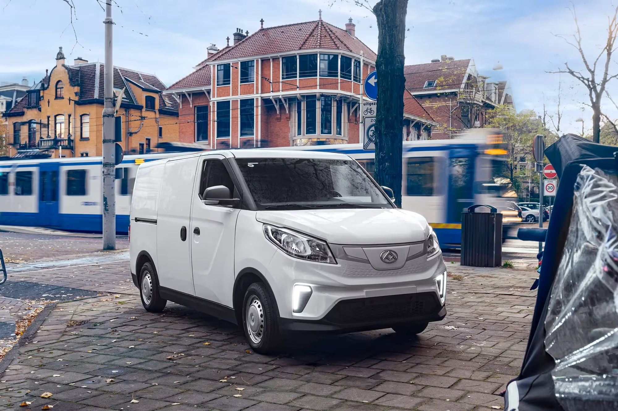 White delivery van parked on a city street with blurred tram and historic brick buildings in the background.