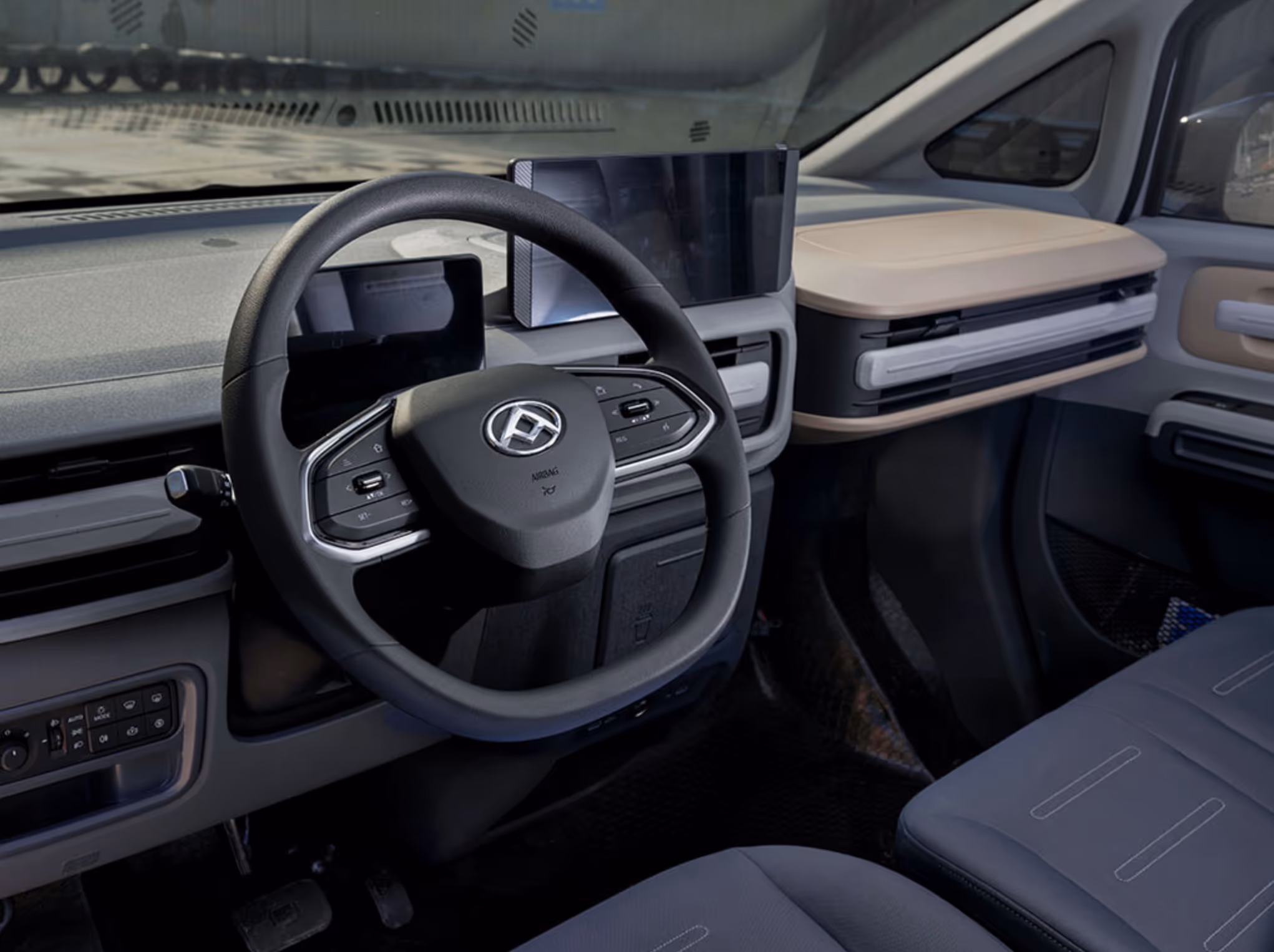 Modern car interior with black multifunction steering wheel, digital instrument panel, touchscreen display, and light beige dashboard storage compartment.