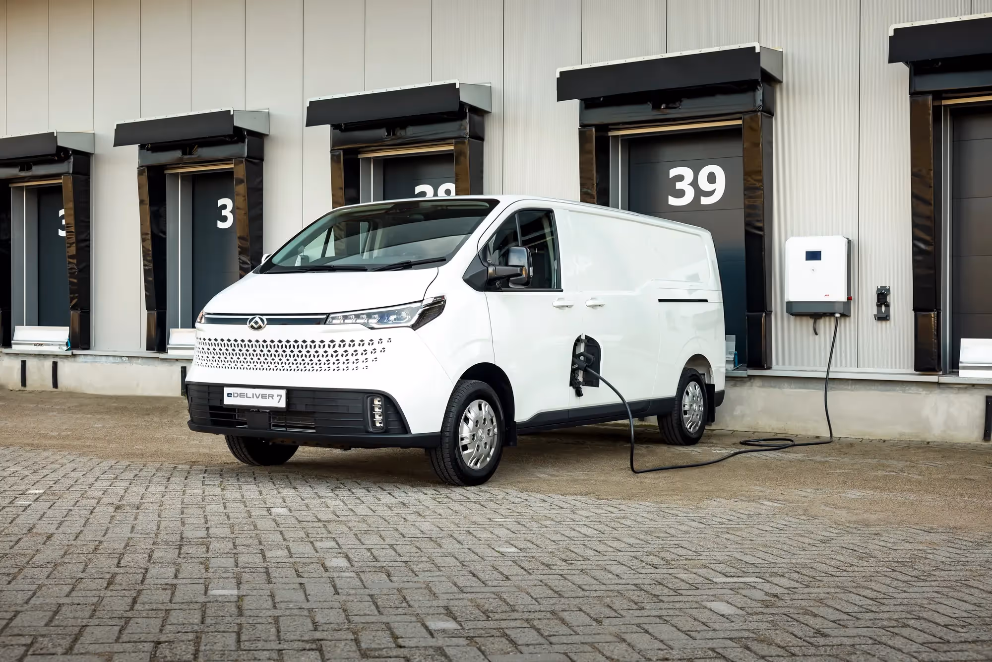 White electric delivery van charging at a dock door numbered 39 in a warehouse.