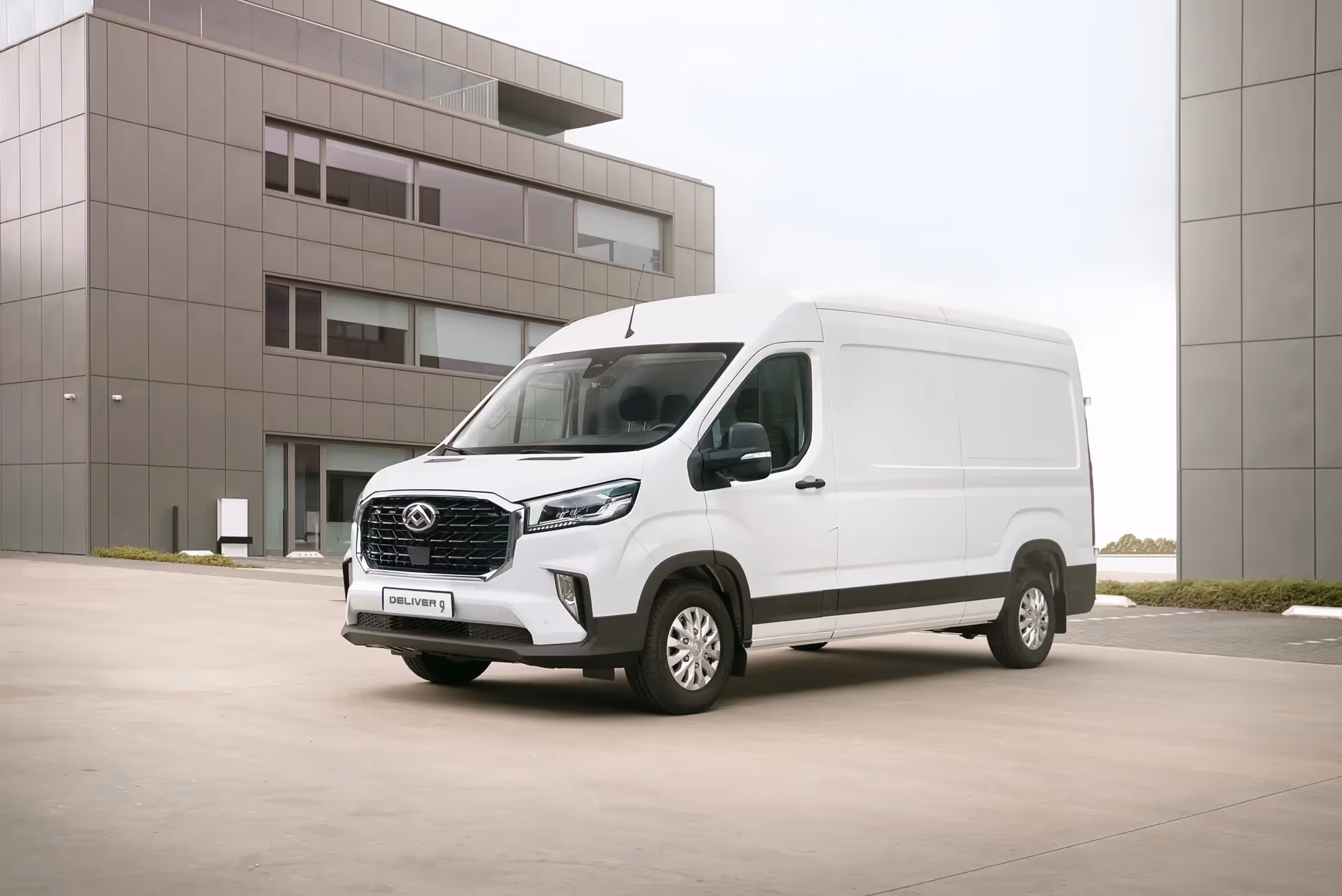 White delivery van parked in front of modern office buildings on a concrete surface.