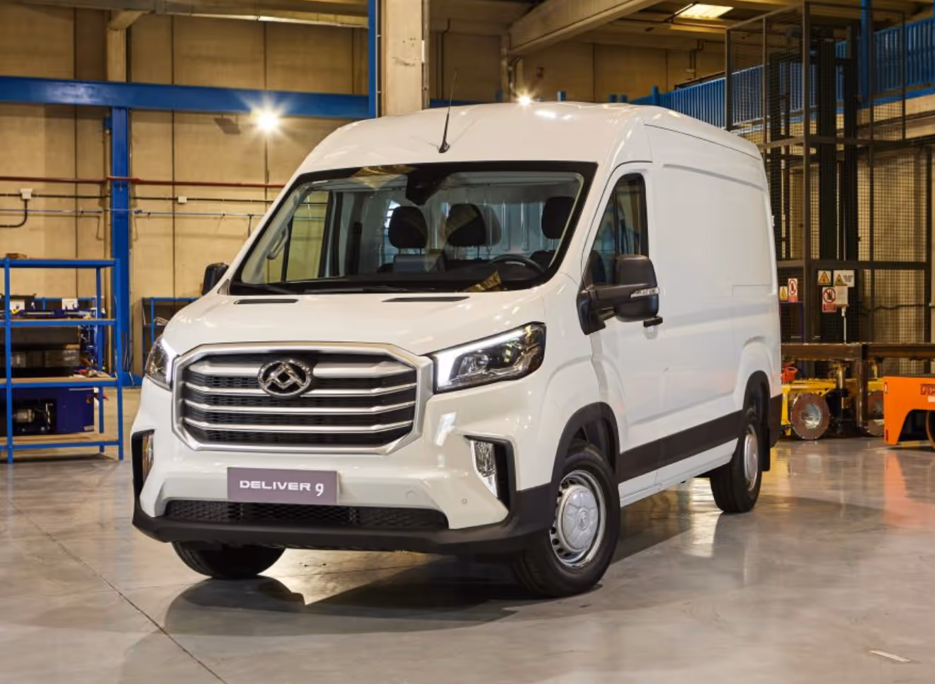 White Deliver 9 cargo van parked inside an industrial warehouse with metal shelves and equipment in the background.