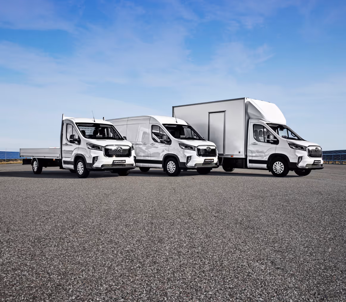 Three white Maxus commercial vehicles lined up on a paved surface under a blue sky.
