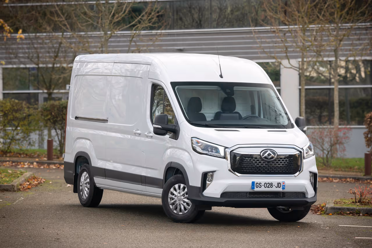 White modern cargo van parked on a suburban street with trees and a building in the background.