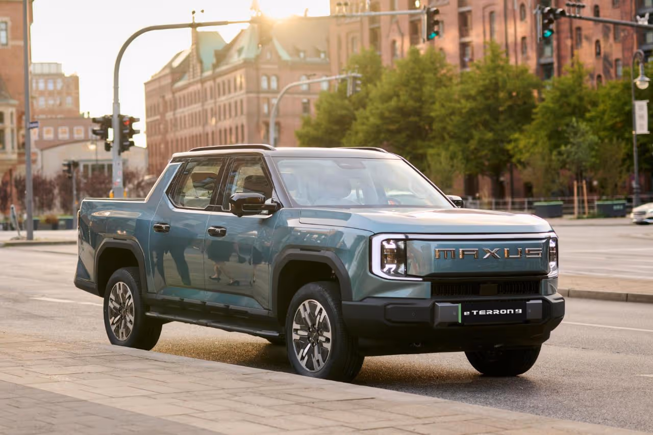 Green Maxus electric pickup truck eTerron 9 parked on a city street at sunset.