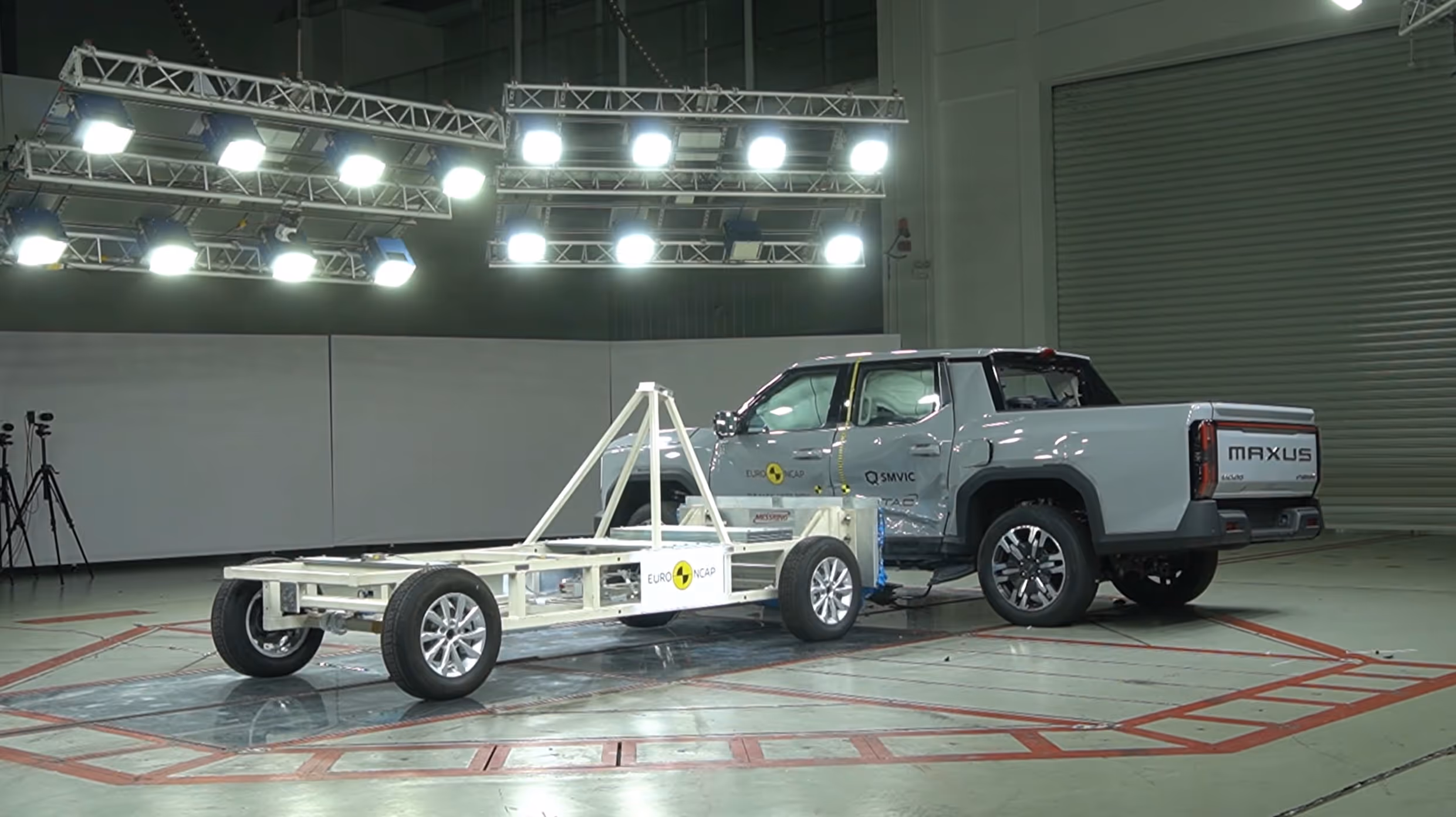 Grey Maxus pickup truck undergoing a side crash test with a mobile barrier inside a test facility.