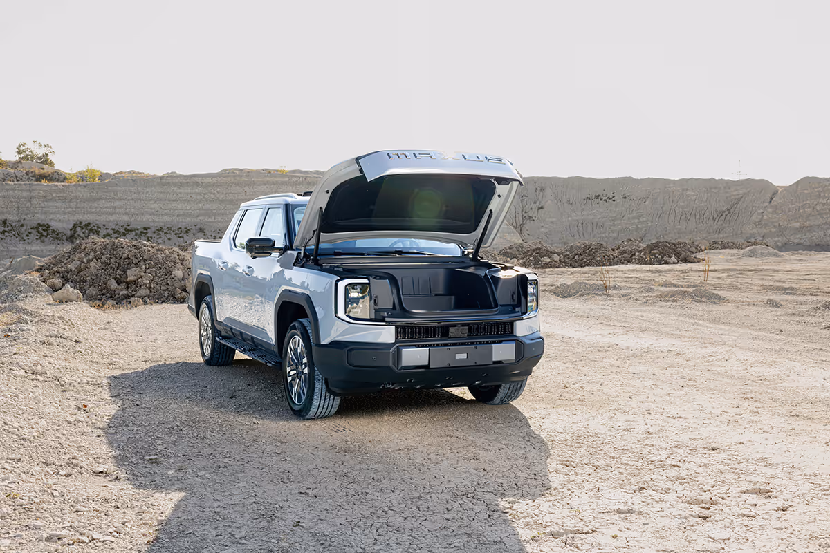 White Rivian electric pickup truck parked on dry dirt with front hood open showing front storage compartment.