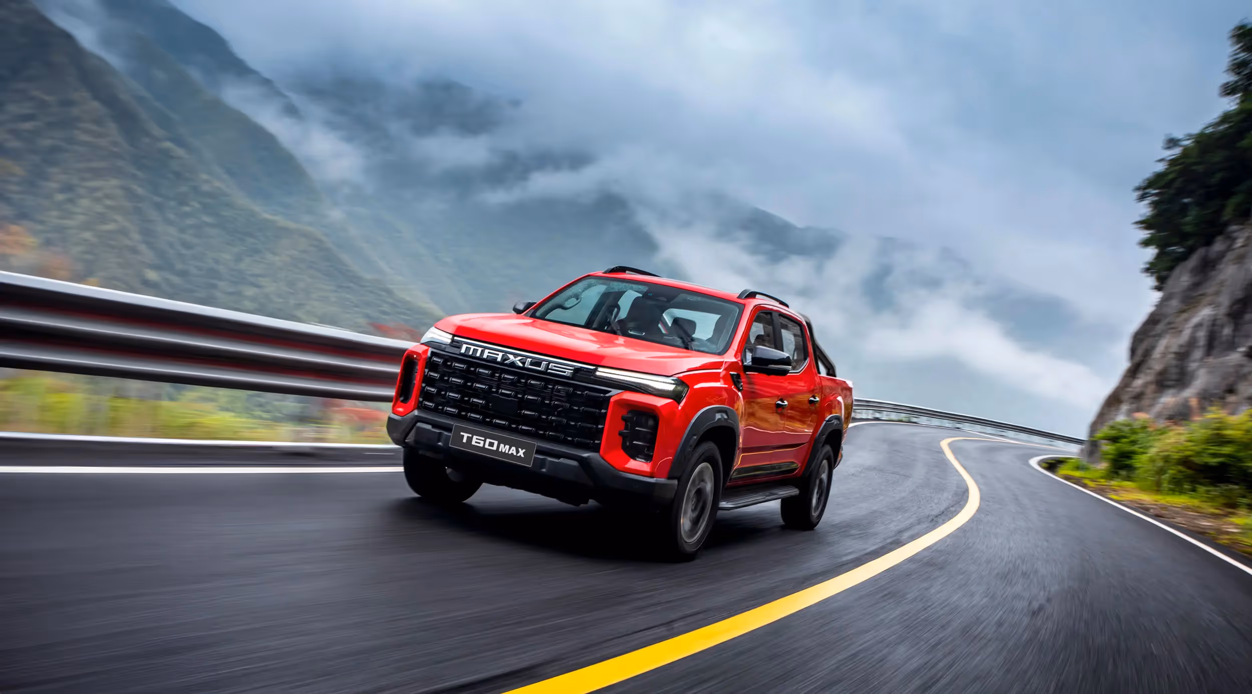 Red Maxus T60 Max pickup truck driving on a winding mountain road with misty hills in the background.