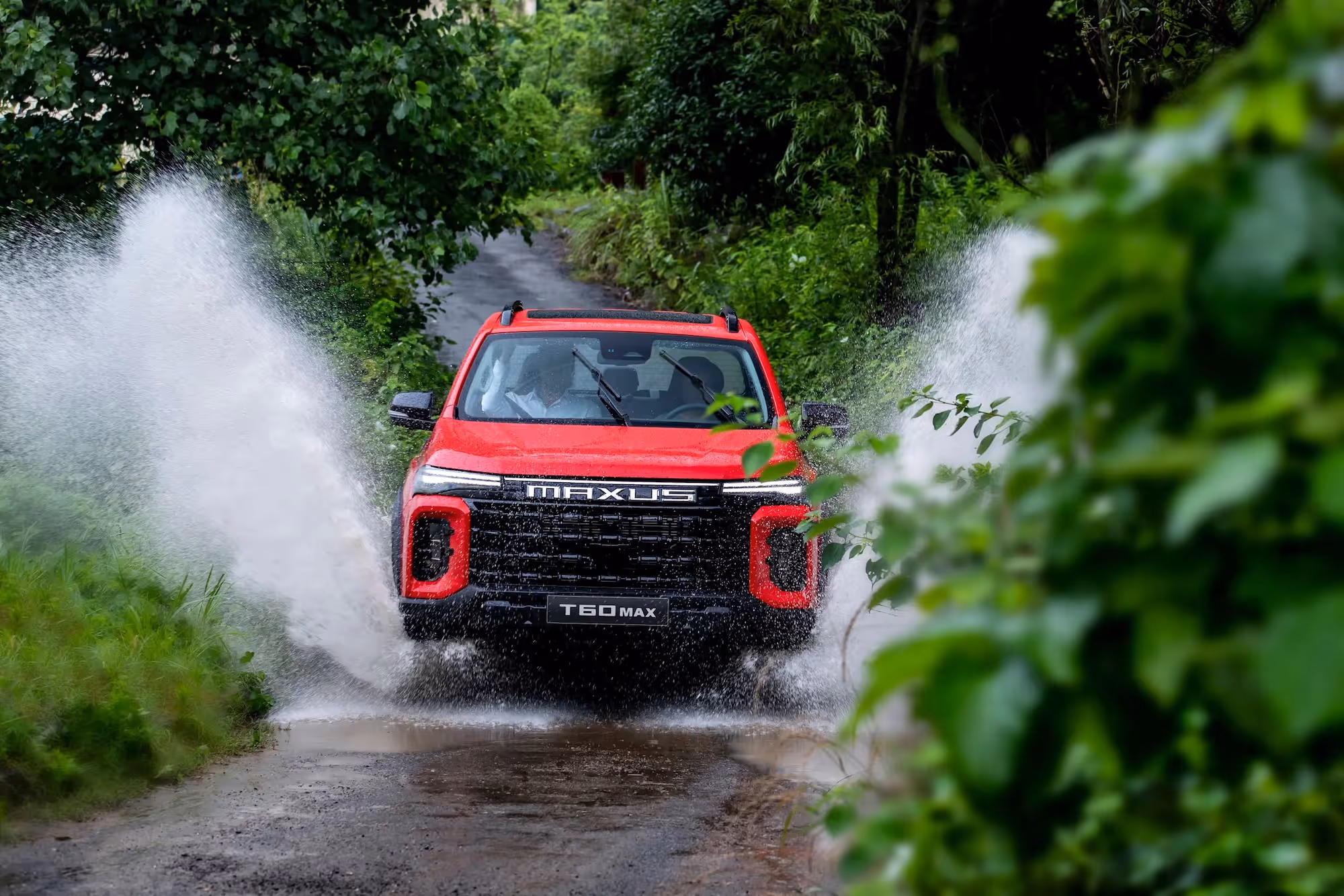 Red Maxus T60 Max pickup truck splashes water while driving on wet forest road.