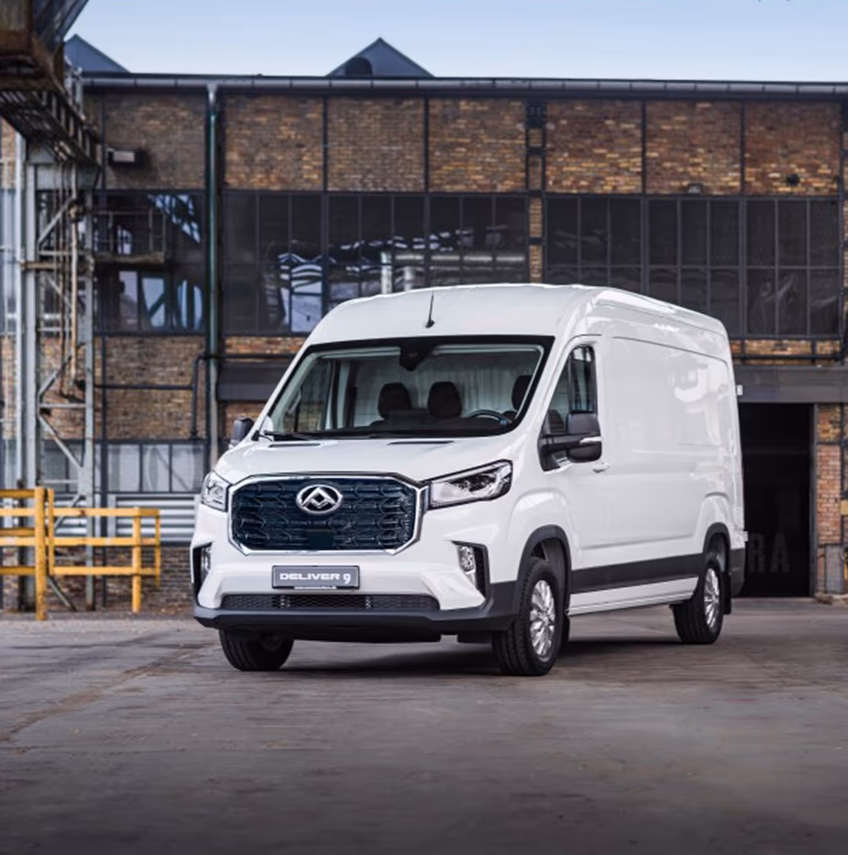 White Maxus Deliver 9 cargo van parked in front of an industrial brick building.