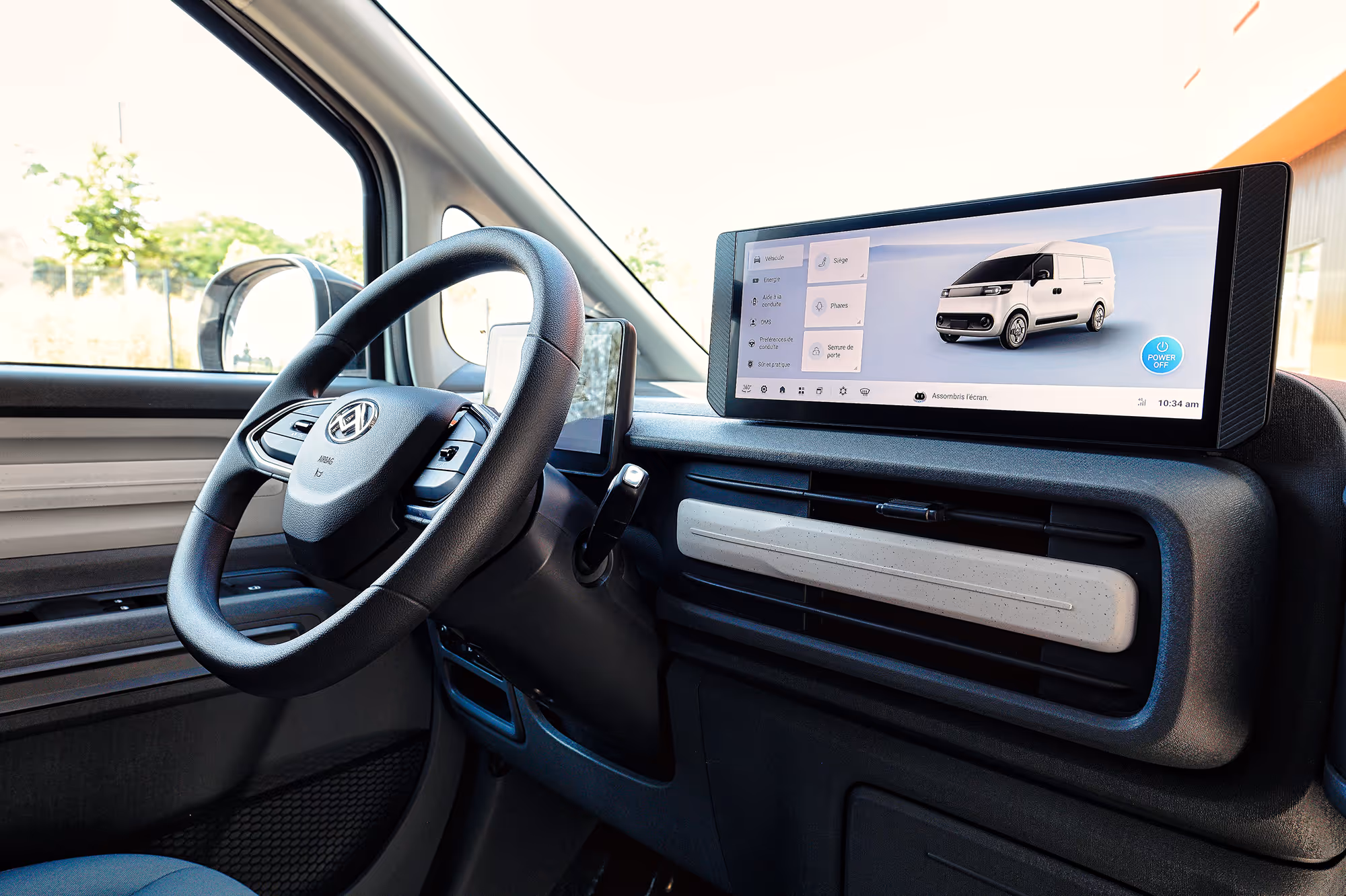 Modern vehicle interior showing steering wheel and wide digital dashboard screen displaying vehicle controls and a white van image.