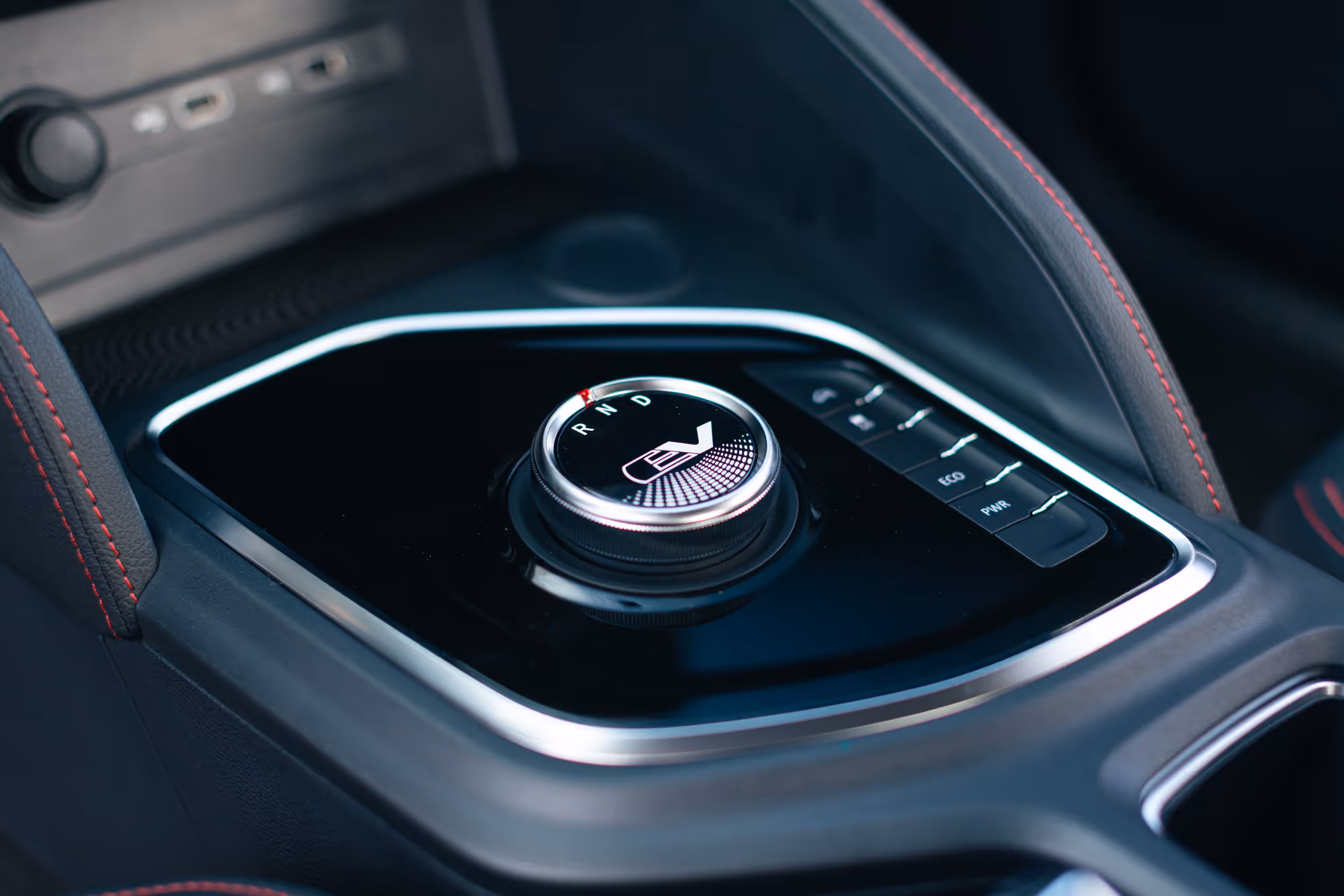 Close-up of an electric vehicle gear selector knob with R, N, D markings and EV logo, surrounded by buttons for ECO and PWR modes.