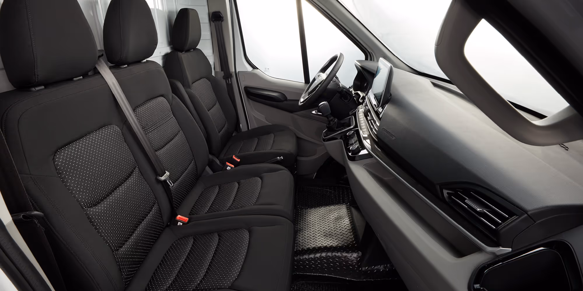 Interior view of a vehicle showing two front seats with black upholstery and patterned inserts, a steering wheel, and a dashboard with a touchscreen display.