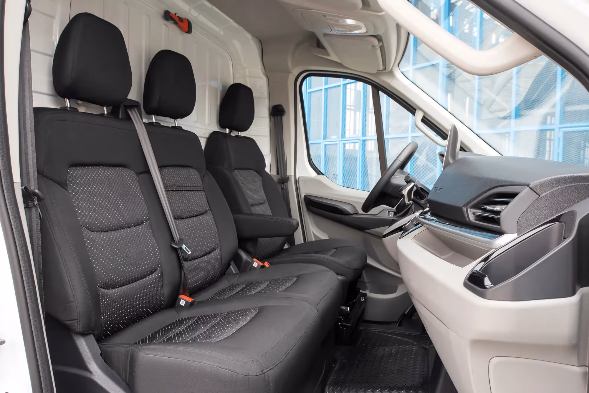 Interior of a delivery van showing a three-seat row with black upholstery and a beige dashboard with steering wheel on the right side.