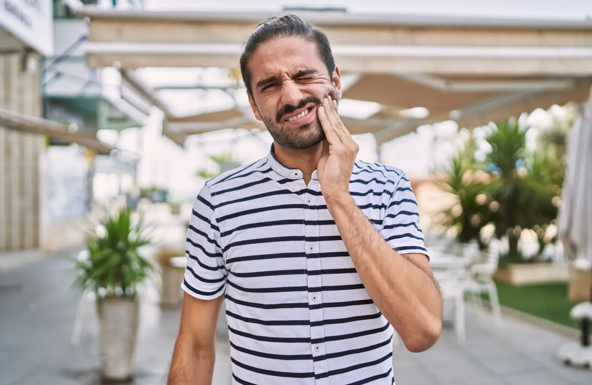 A man in a striped shirt is holding his hand to his face.